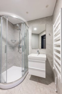 Çağdaş banyo, cam kaplı bir duş, parlak beyaz bir lavabo dolabı, gri fayanslı duvarlar, ve temiz ve minimalist bir tasarımla modern konforlar..