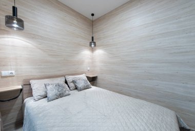 Doğal ahşap aksanları, yorgan örtülü yatak örtüsü ve ortam ışıkları olan şık ve sakin bir yatak odası, rahat ve davetkar bir atmosfer yaratıyor. Modern Minimalist Ev Yatak Odası İçi