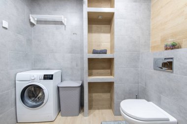 İyi düzenlenmiş bir alanda çok işlevli bir araç sunmak için çamaşır makinesi, tuvalet ve ahşap bölme rafları olan temiz ve şık bir banyo. Modern Ev Banyosu İçi
