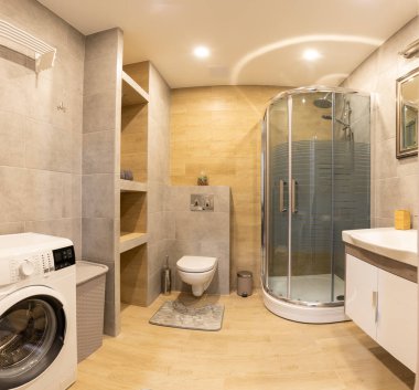 Küçük bir duş kabini, çamaşır makinesi ve zarif mobilyaları olan, ahşap ve gri kiremitlerle tamamlanmış sıcak ve davetkar bir parlaklığı olan çağdaş bir banyo. Modern Ev