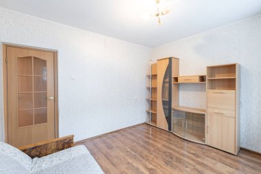 Ahşap dolaplar, bir kanepe ve doğal ışık için geniş bir pencerenin olduğu basit ve parlak bir oturma odası. Modern dekor minimalizm ve işlevselliği vurguluyor.