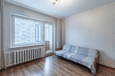 Ahşap dolaplar, bir kanepe ve doğal ışık için geniş bir pencerenin olduğu basit ve parlak bir oturma odası. Modern dekor minimalizm ve işlevselliği vurguluyor.