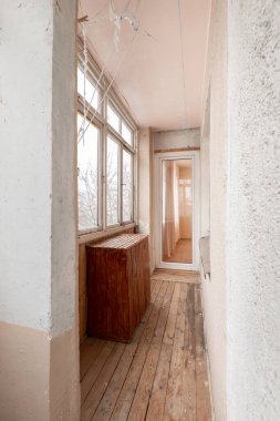 Enclosed balcony with large windows offering a view, featuring wooden paneling and flooring, located in an urban apartment building. Old Soviet Style Home Interior clipart