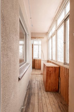 Enclosed balcony with large windows offering a view, featuring wooden paneling and flooring, located in an urban apartment building. Old Soviet Style Home Interior clipart