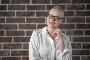 Kafası tıraşlı, güzel, beyaz bir kadının portresi. Kanserden kurtulan bir kadın. Gözlüklü Gülümseyen Kadın, Stüdyo ortamında güven içinde poz veriyor. Bir portre dayanıklılık gösterisi. Gülümse.