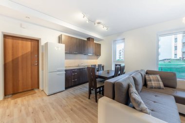 Açık bir mutfak, yemek alanı ve rahat bir oturma odası olan iyi ışıklandırılmış modern bir daire. Modern Ev Açma Planı Mutfağı ve Oturma Odası İçi Yemek Masası ve Pencere Görünümü.