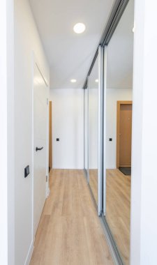 Ahşap döşeme, beyaz bir kapı ve aynalı gardırop kapılarının olduğu parlak ve çağdaş bir koridor tasarımı. Ahşap döşemeli modern koridor. İskandinav Tarzı