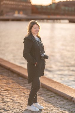 Gün batımında bir nehrin kenarında elinde kamerayla bekleyen bir kadın yaratıcılık ve neşe saçıyor. Şehir Merkezinde Sunset 'te Mutlu Fotoğrafçılar Rıhtımda Duruyor. Kopenhag, Danimarka
