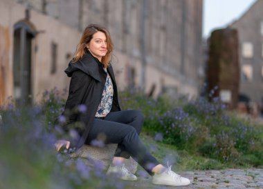 Taştan bir yüzeyde oturan bir kadın çiçek açan lavantalarla çevrili, arka planda tarihi bir binayla şehir dışında huzurlu bir anın tadını çıkarıyor. Kopenhag Şehri, Danimarka