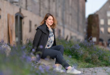 Taştan bir yüzeyde oturan bir kadın çiçek açan lavantalarla çevrili, arka planda tarihi bir binayla şehir dışında huzurlu bir anın tadını çıkarıyor. Kopenhag Şehri, Danimarka