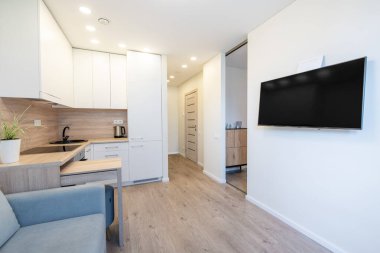 Beyaz dolaplar, ahşap aksanlar ve gösterişli bir televizyonla donatılmış parlak ve modern bir mutfak. Bu alan, çağdaş yaşam tarzları için işlevsellik ve estetik cazibeyi birleştirir..