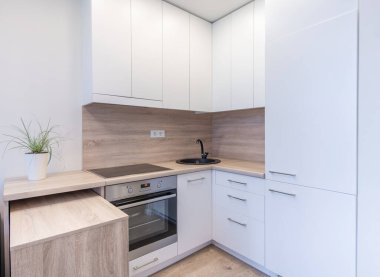 Parlak beyaz dolaplar, ahşap tezgah ve modern aletlerin yer aldığı çağdaş bir mutfak tasarımı. Bir bitki biraz yeşillik katar, her ev için temiz ve işlevsel tarzı tamamlar.