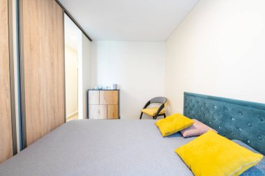 Parlak ve modern yatak odası, minimalist mobilyaları ve rahat dekorlarıyla çağdaş tasarımı sergiliyor, canlı yastıklı rahat bir yatak, ahşap döşeme, büyük pencerelerden gelen doğal ışık