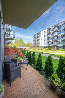 Ahşap bir güvertede sandalyeli balkon manzaralı bahçeler ve modern daireler..