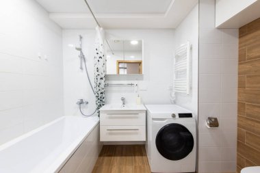 Duş küveti, çamaşır makinesi, lavabo ve ahşap aksanları olan parlak ve temiz ev banyosu işlevsellik ve estetik çekiciliği küçük bir alanda birleştiriyor..