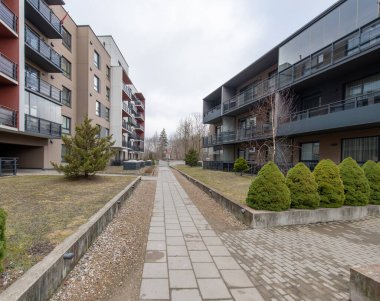 Çok katlı balkonların, manzaralı yeşilliklerin ve bulutlu bir günde banliyöde kaldırımlı yaya yolunun bulunduğu çağdaş konut binaları..