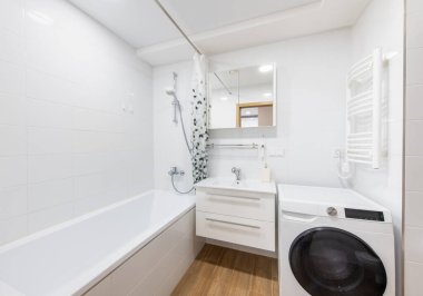 Küvet, çamaşır makinesi, depolanmış lavabo ve açık renk palet içeren parlak ve çağdaş banyo tasarımı. Uzay modern evler için temiz ve işlevsel bir estetik ideal sergiliyor..