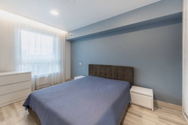 Mavi duvarları, şık mobilyaları ve sakin bir atmosferi olan parlak ve çağdaş bir yatak odası. Mekan doğal ışıkla aydınlanmış ve modern iç estetik sergiliyor..