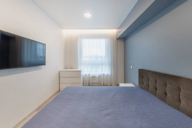 Parlak yatak odasının içinde modern bir tasarım, rahat bir yatak odası, televizyon ve şeffaf perdelerin arasından geçen doğal bir ışık var. Rahatlamak ve rahatlamak için ideal barışçıl ve minimalist bir düzen..