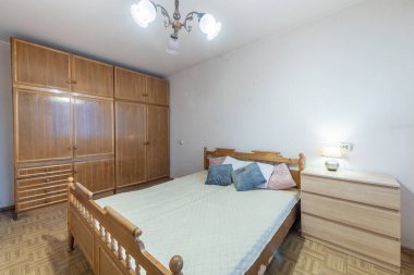 Parlak ve kırsal yatak odası ahşap bir gardırop, yatak çerçevesi ve komodiniyle uyumlu yumuşak yastıklar ve sıcak ışıklandırmayla süslenmiş, sükunet ve basit ev mobilyaları için ideal..