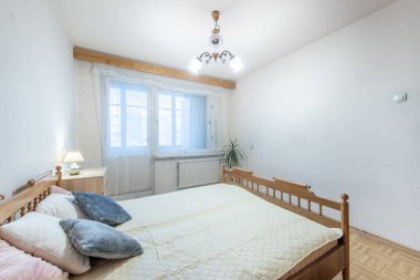 Parlak yatak odasının içinde ahşap yatak çerçevesi, yumuşak tekstil, saksı bitkisi ve büyük pencerelerden gelen doğal ışıklandırma var. Dekorasyon, rahatlatıcı ev ortamları ya da mimari ilham için mükemmel