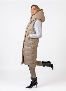 Bej giyimli ve siyah topuklu giyen neşeli bir kadın dinamik bir şekilde kendine güvenerek poz veriyor..