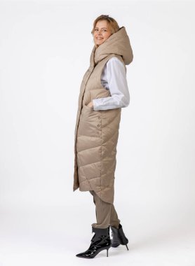 Bej giyimli ve siyah topuklu giyen neşeli bir kadın dinamik bir şekilde kendine güvenerek poz veriyor..