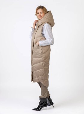 Bej giyimli ve siyah topuklu giyen neşeli bir kadın dinamik bir şekilde kendine güvenerek poz veriyor..