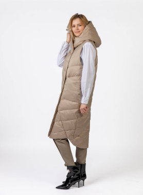 Bej giyimli ve siyah topuklu giyen neşeli bir kadın dinamik bir şekilde kendine güvenerek poz veriyor..