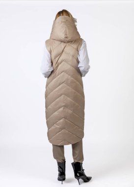 Bej giyimli ve siyah topuklu giyen neşeli bir kadın dinamik bir şekilde kendine güvenerek poz veriyor..