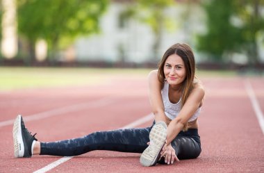 Spor giyimli genç ve mutlu bir kadın açık havada esneme hareketleri yapıyor. Neşeli görünüyor, aktivitelerinden ve yeşil manzaralı çevresinden hoşlanıyor, fitness ve aktif bir yaşam tarzını destekliyor..