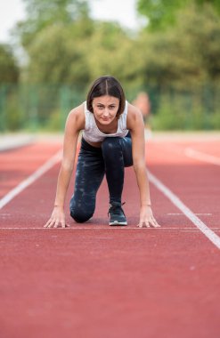 Açık bir pistte koşuya hazırlanan konsantre bayan sporcu başlangıç pozisyonunda..