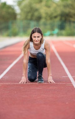 Açık bir pistte koşuya hazırlanan konsantre bayan sporcu başlangıç pozisyonunda..