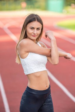 Genç, beyaz bir kadın atletizm pistinde geriniyor, formda ve sağlıklı bir hayat sürüyor..