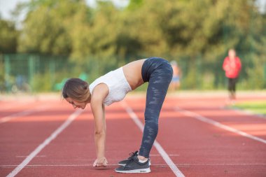 Spor giyimli genç ve mutlu bir kadın açık havada esneme hareketleri yapıyor. Hareketli bir parktaki koşu pistinde esneklik egzersizleri yapan aktif genç bir kadın..