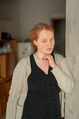 Kapalı alanda uzun kızıl kızıl saçlı, güzel ve barışçıl ifadesini vurgulayan genç bir kadını gösteren sakin bir portre..