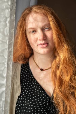 Kızıl saçlı, koyu renkli benekli bir kıyafet giyen, yumuşak pencere ışığıyla aydınlanan ve doğal gölgeler yaratan beyaz bir kadının yakın plan portresi. Rahatlamış bir ifade yakalar