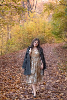 Beyaz, beyaz, şık bir elbise giymiş, paltolu bir kadın turuncu ve sarı yapraklarla çevrili, canlı bir sonbahar yolunda yürüyor..