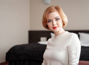 Şık, beyaz, beyaz, parlak kırmızı rujlu ve mükemmel bir saç stili olan bir Kehanet. Kapalı bir yerde oturuyor, kendine güven ve özgüven saçıyor. Yumuşak arkaplan resme sade ve rahat bir ortam ekler.