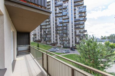 Çağdaş apartmanların ve yakınlardaki alışveriş alanının parlak ve geniş balkon manzarası, kentsel gelişimi ve konforlu yaşamı vurguluyor