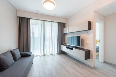 Konforlu bir kanepe, minimal mobilyalar ve yatak odasına açılan kapının yanında duvara monte edilmiş bir televizyon olan çağdaş, parlak bir oturma odası..