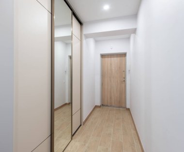 Ahşap kapılı, döşemeli ve minimalist ve işlevsel bir estetik sunan aynalı gardırobu olan parlak ve modern ev koridoru.
