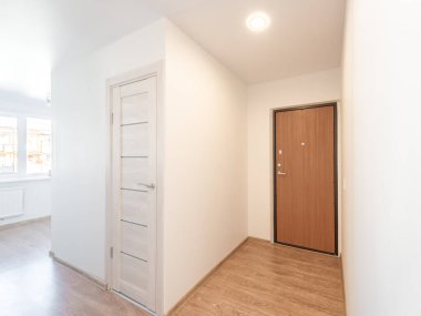 Parlak ve işlevsel apartman koridorunda ahşap zemin, floş kapılar ve doğal, minimalist bir dekor var.