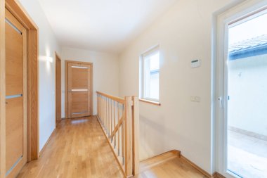 Ahşap zemin ve kapılı parlak modern koridor, minimalist tasarım ve doğal ışıklandırma sergileniyor..