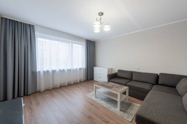 Parlak, çağdaş oturma odasında gri bir kanepe, perdeli büyük pencereler ve ahşap döşemeler var. Şehir içi ve ev dekorasyonu için mükemmel bir konfor ve tarz dengesi..