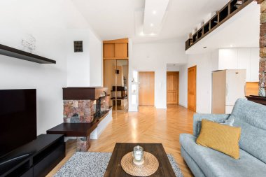 Parlak ve ferah oturma odasında ahşap zeminler, şömine, beyaz duvarlar ve minimalist dekorlar var. Rahatlama ya da çağdaş yaşam tarzı temsili için ideal konforlu ve davetkar iç uzay.