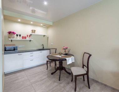 İçinde kompakt mutfak düzeneği, iki kişilik yemek masası ve yumuşak ışıklandırmalı şık sandalyeler olan rahat, modern bir iç mekan. Modern Kuyu Işığı İçi Yemek Masası ile Küçük Ev Mutfağı