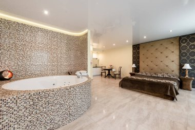 Bir yatak odası, fayanslı jakuzi alanı ve rahat mutfak düzeneği olan şık bir otel odası tasarımı. Geniş Otel Suitinde Yatak Odası, Jakuzi ve Mutfak ile Modern Ev İçi