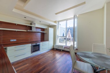 Zarif açık-planlı mutfak iç mimarisi gösterişli dolaplar, ahşap döşemeler ve geniş pencerelerden süzülen doğal ışık açık hava terası manzaralı..