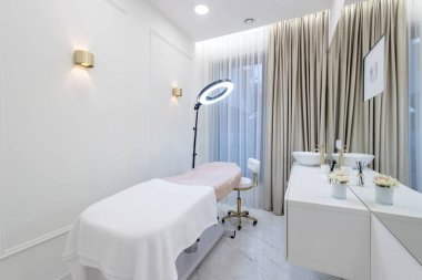 Zarif ve minimalist bir spa odası. Tedavi masası, halka ışığı ve sakin bir ortam..